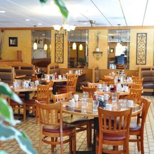 A cozy restaurant interior with wooden tables, chairs, and a warm color scheme, set for dining.