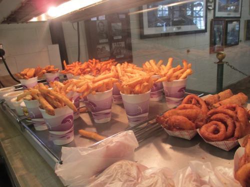 A display of various fried foods, including French fries in cups and onion rings on a tray.