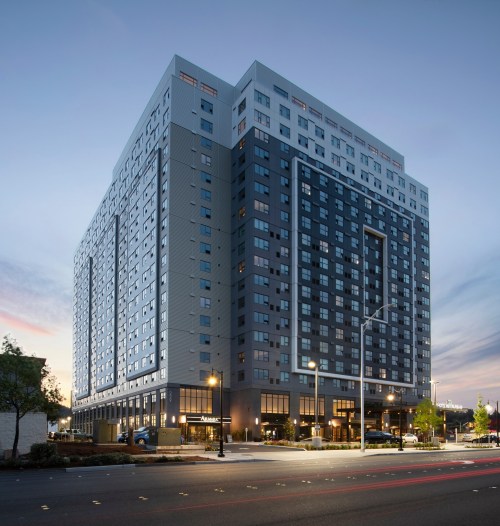 Modern high-rise building at dusk, featuring large windows and a sleek design, with streetlights illuminating the area.