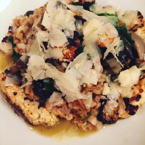 A plate of roasted cauliflower topped with grains, greens, and shaved cheese, drizzled with a light sauce.