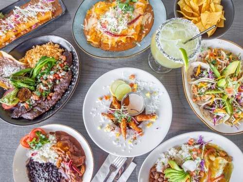 A vibrant spread of Mexican dishes, including enchiladas, tacos, rice, beans, and a margarita, arranged on a table.