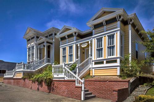A charming yellow house with white trim, featuring multiple gables and a front staircase, set against a blue sky.