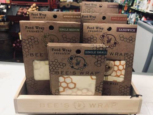 A wooden display holds various sizes of Bee's Wrap reusable food wraps, labeled for different uses like sandwiches and bread.