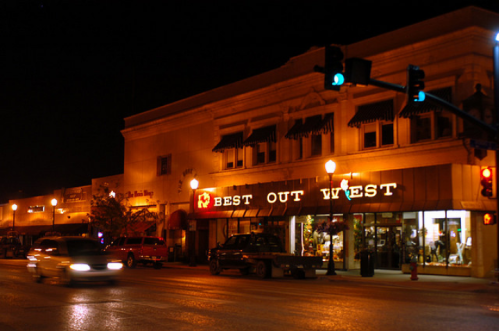 Nighttime street view featuring a store named "Best Out West" with illuminated signs and parked cars.