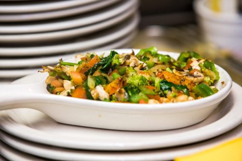 A white dish filled with a colorful mix of sautéed vegetables, including broccoli, tomatoes, and green peppers.