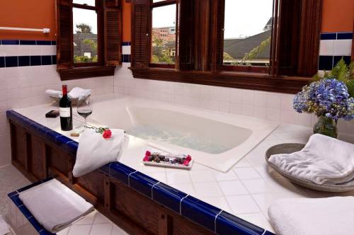 A luxurious bathroom with a large tub, wine, flowers, and towels, surrounded by wooden windows and colorful tiles.