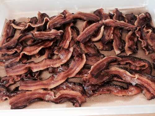 A tray of crispy, cooked bacon strips arranged neatly on a paper towel.