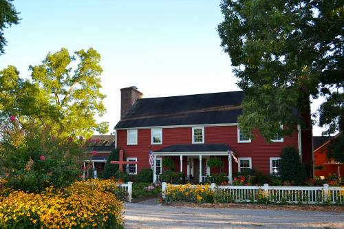 A charming red house surrounded by colorful flowers and greenery, with a clear blue sky in the background.