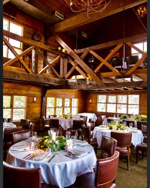 Cozy wooden restaurant interior with elegant tables set for dining, featuring a lofted area and large windows.