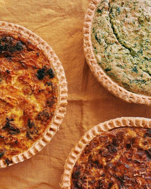 Three savory pies on a golden cloth: a broccoli pie, a spinach pie, and a cheese pie, each in a flaky crust.