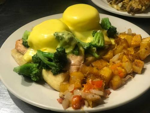 A plate of eggs Benedict with broccoli, topped with hollandaise sauce, served with seasoned roasted potatoes.