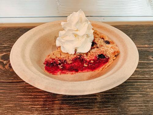 A slice of berry pie topped with whipped cream on a paper plate, resting on a wooden table.