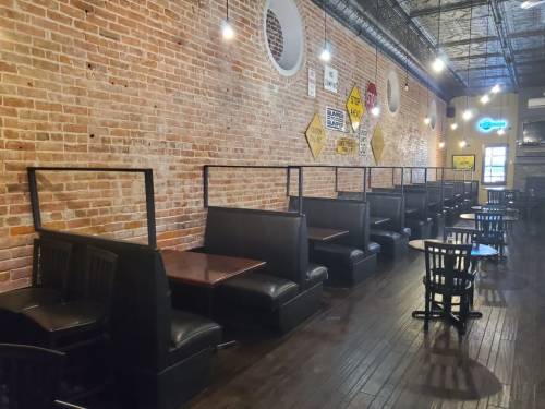 Interior of a restaurant featuring brick walls, black booths, and wooden tables under warm lighting.