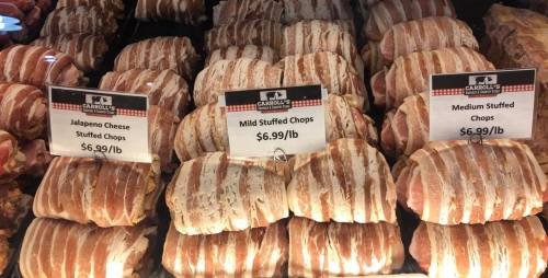 Display of various stuffed pork chops wrapped in bacon, with price tags for jalapeño cheese, mild, and medium options.