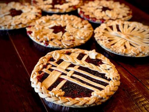 A variety of beautifully decorated fruit pies with intricate crust designs on a wooden table.