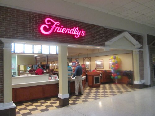 A Friendly's restaurant in a mall, featuring a bright sign, checkered floor, and colorful balloons nearby.