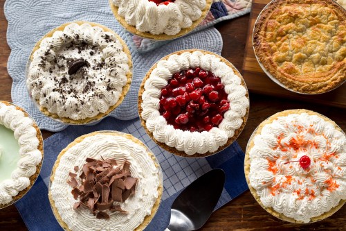 A variety of decorated cakes with whipped cream, chocolate, cherries, and orange sprinkles on a wooden table.