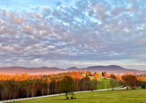 A scenic landscape featuring rolling hills, colorful autumn trees, and a cloudy sky at sunset.