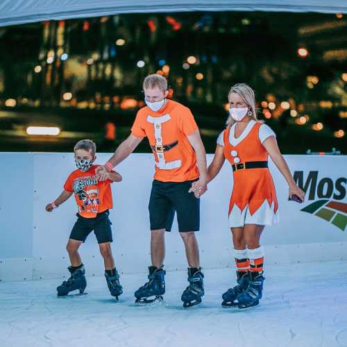 A family ice skating together, wearing festive outfits and masks, enjoying a fun winter activity.