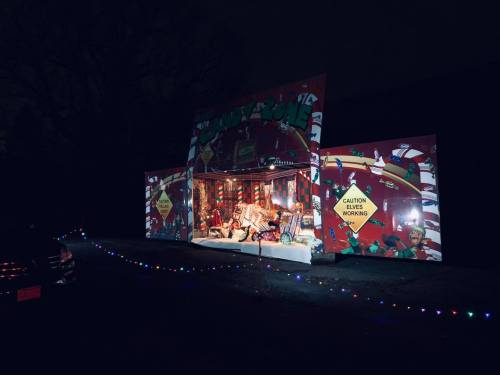 A festive display with colorful lights and decorations, featuring a sign that says "Caution: Elves Working."