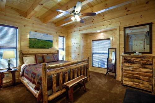 Cozy wooden bedroom with a log bed, dresser, and large windows, featuring rustic decor and warm lighting.