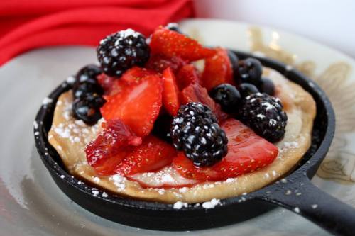 A skillet dessert topped with fresh strawberries, blackberries, and blueberries, dusted with powdered sugar.