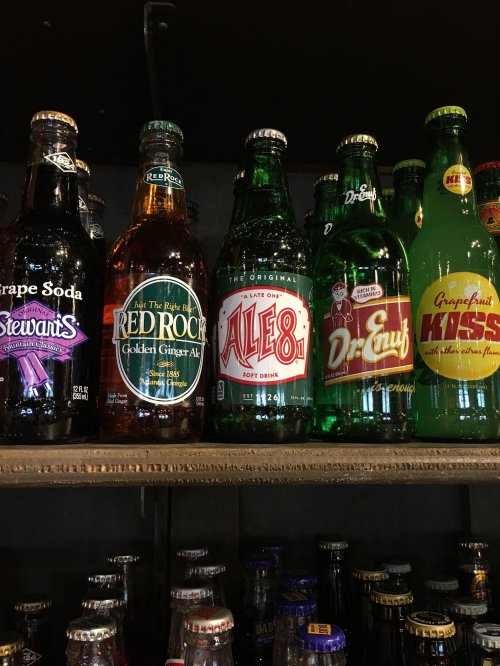 A shelf displaying various vintage soda bottles, including grape soda, ginger ale, and Ale-8-1.