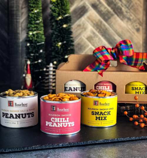 A display of bourbon smoked snacks, including peanuts and chili peanuts, in colorful cans and a snack mix box.