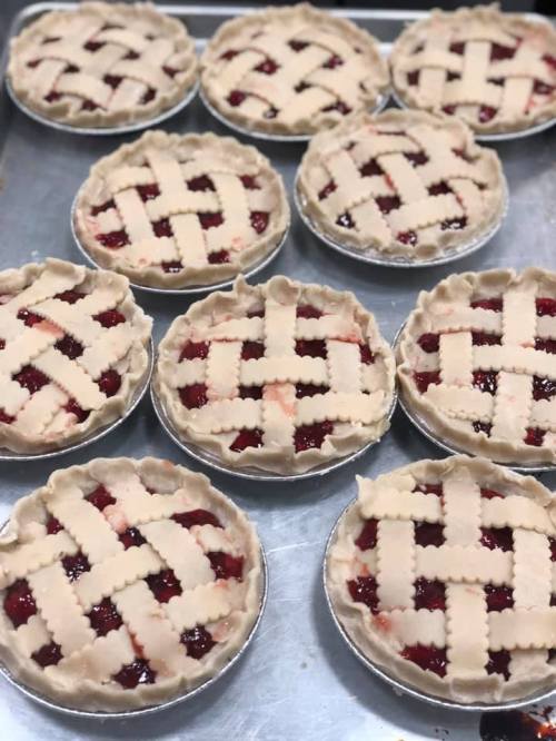 A tray of freshly prepared mini fruit pies with lattice crusts, ready for baking.