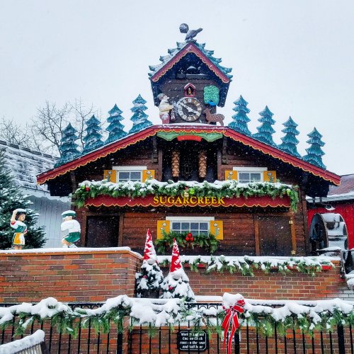 A charming wooden building with a clock tower, decorated for the holidays, surrounded by snow and evergreen trees.