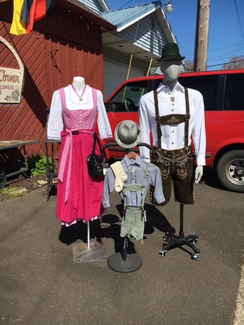 Two mannequins display traditional German outfits: a dirndl and lederhosen, with a child's outfit in between.