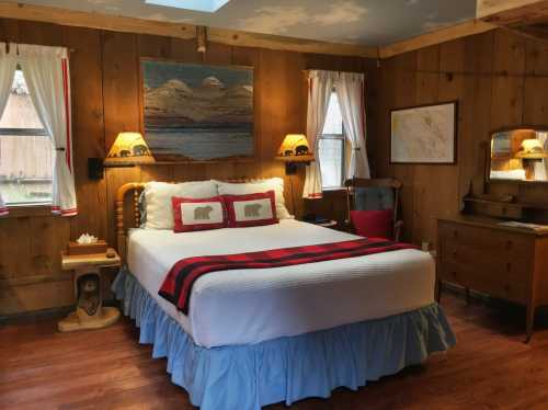 Cozy wooden bedroom with a double bed, plaid blanket, and rustic decor, featuring a painting and warm lighting.