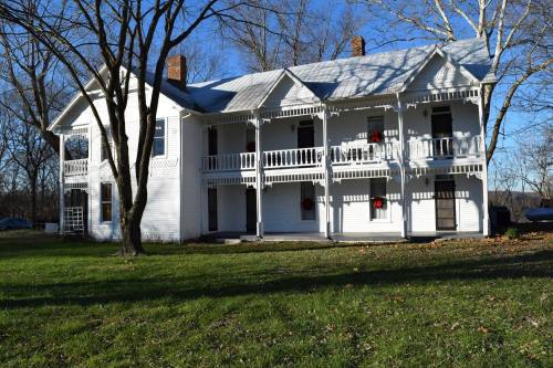 A two-story white house with balconies, surrounded by trees and grass on a sunny day.