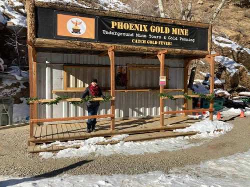 A person stands at the entrance of the Phoenix Gold Mine, surrounded by snow and festive decorations.