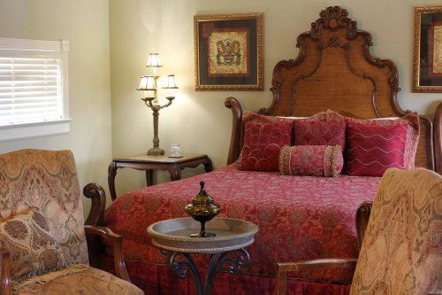 Cozy bedroom featuring a wooden bed with red bedding, two patterned chairs, and decorative lamps.