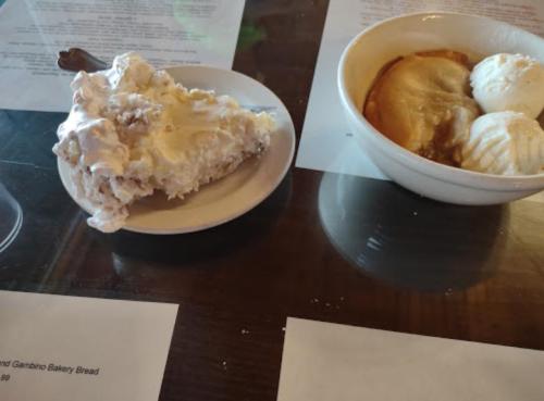 A plate with a slice of dessert topped with cream next to a bowl of ice cream and a pastry on a table.
