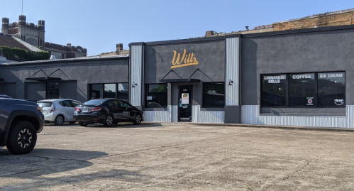 Exterior of a gray building with "Wills" sign, featuring a parking lot and windows displaying coffee and ice cream.