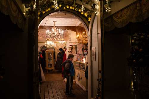 A cozy, festive shop entrance decorated with lights and snowflakes, featuring a child exploring inside.