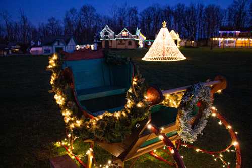 A decorated sleigh with lights in a festive setting, featuring a glowing Christmas tree and illuminated buildings in the background.