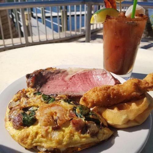 A plate with an omelet, fried chicken, and a slice of meat, alongside a drink with garnishes.