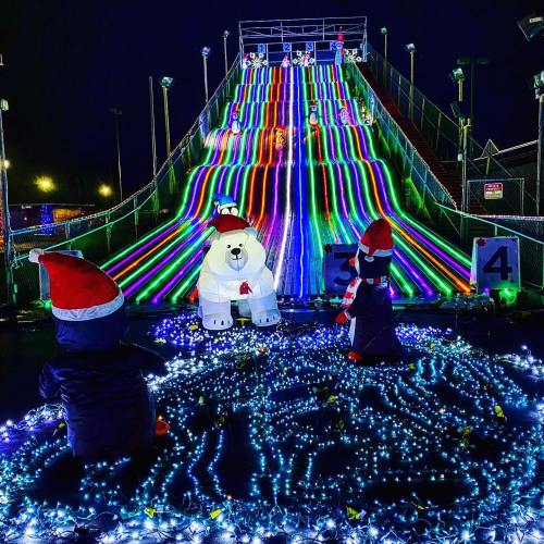 Colorful illuminated slide at night, featuring a polar bear and penguin decorations in festive hats, surrounded by lights.