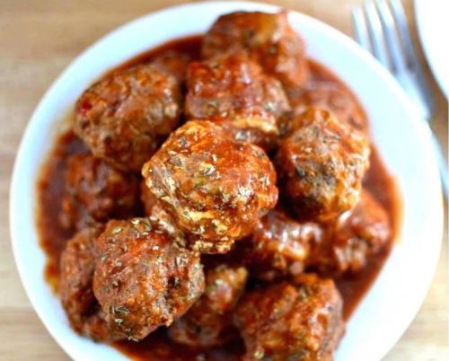 A bowl of meatballs covered in rich tomato sauce, garnished with herbs.