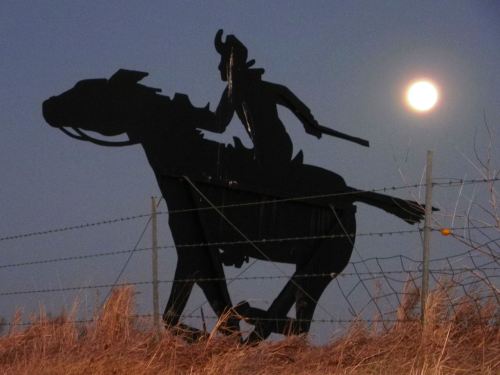 Silhouette of a cowboy on horseback against a night sky with a full moon.