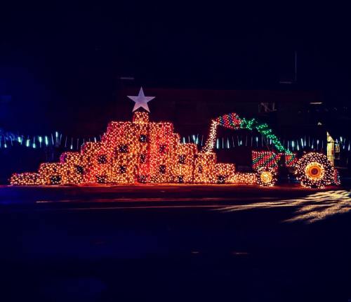 A festive display of colorful lights shaped like a tractor and a pyramid, topped with a star, set against a dark night sky.