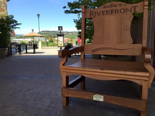 A large wooden chair labeled "Napa's Riverfront" sits in a plaza with trees and a view of the river in the background.