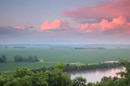 A serene landscape featuring lush green fields, a winding river, and colorful clouds at sunset.