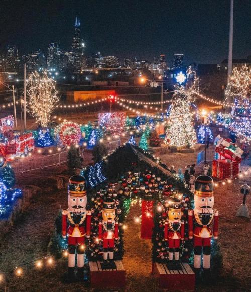 A festive holiday display featuring lights, nutcracker figures, and decorated trees against a city skyline at night.
