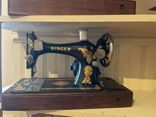 A vintage Singer sewing machine displayed on a shelf, featuring ornate designs and a wooden base.