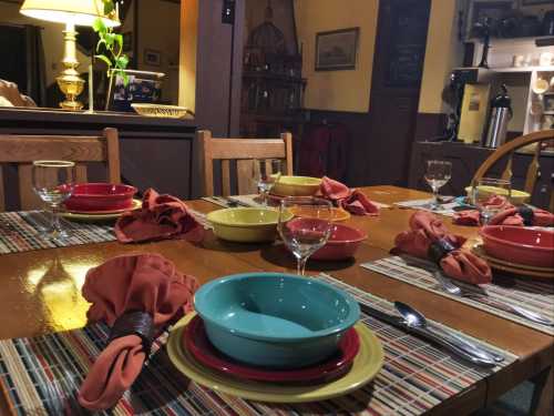 A dining table set with colorful plates, bowls, and glasses, surrounded by warm lighting and a cozy atmosphere.