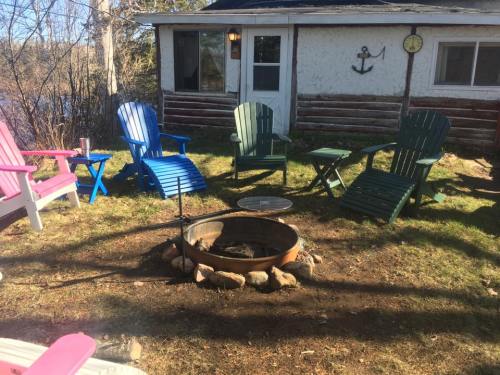 A cozy outdoor seating area with colorful chairs around a fire pit, near a cabin by the water.